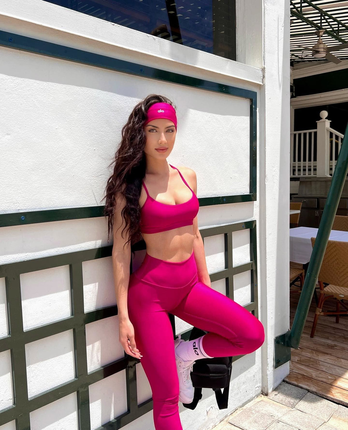 @georginamazzeo wearing a hot pink sports bra with a matching pair of hot pink high-waisted leggings while posing against a white wall.